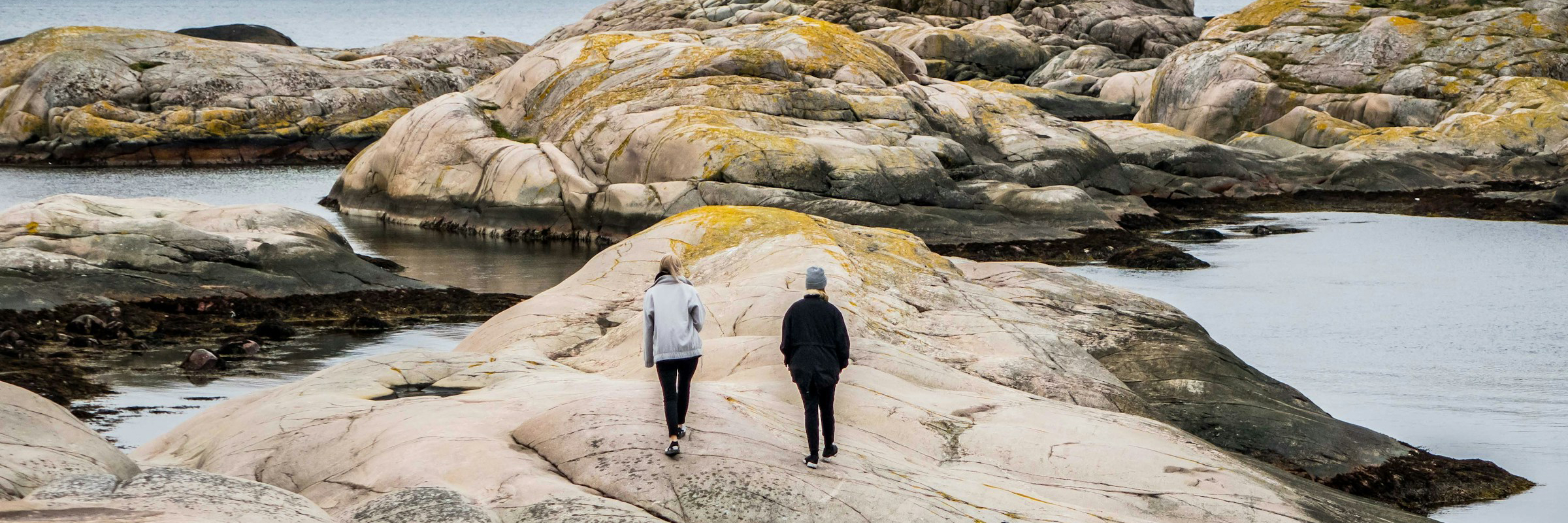 Zwei Personen gehen über Felsen, die von Wasser gesäumt sind.