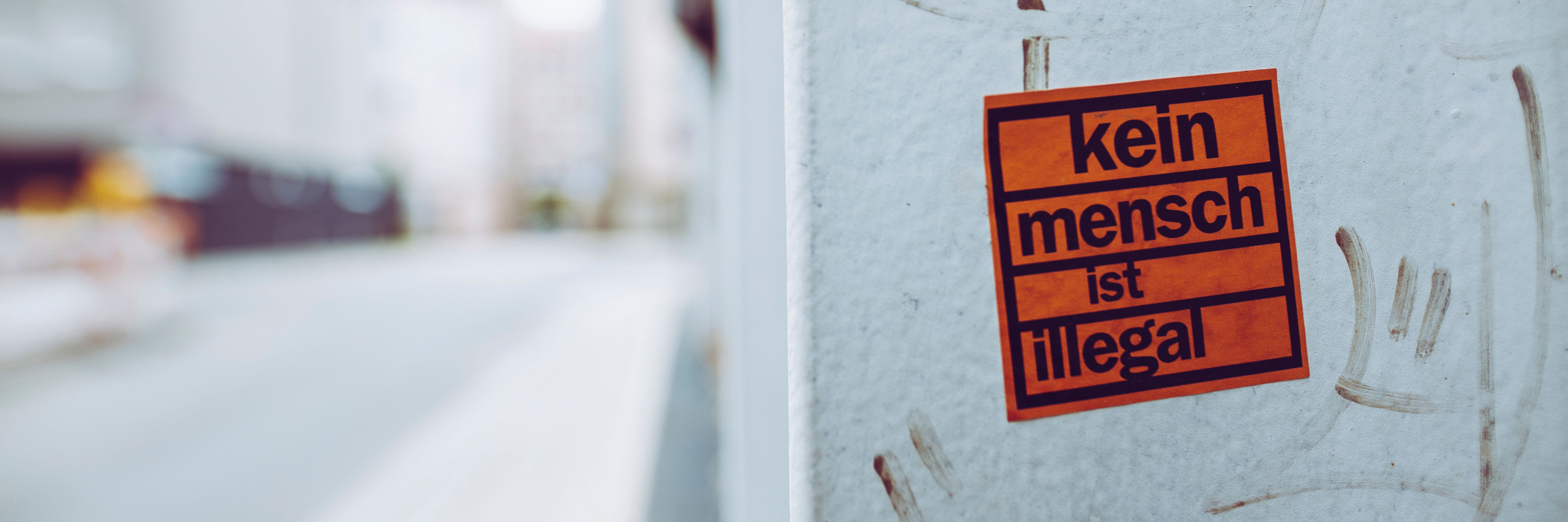 Ein Aufkleber mit der Aufschrift "Kein Mensch ist illegal" klebt an einer Hauswand.
