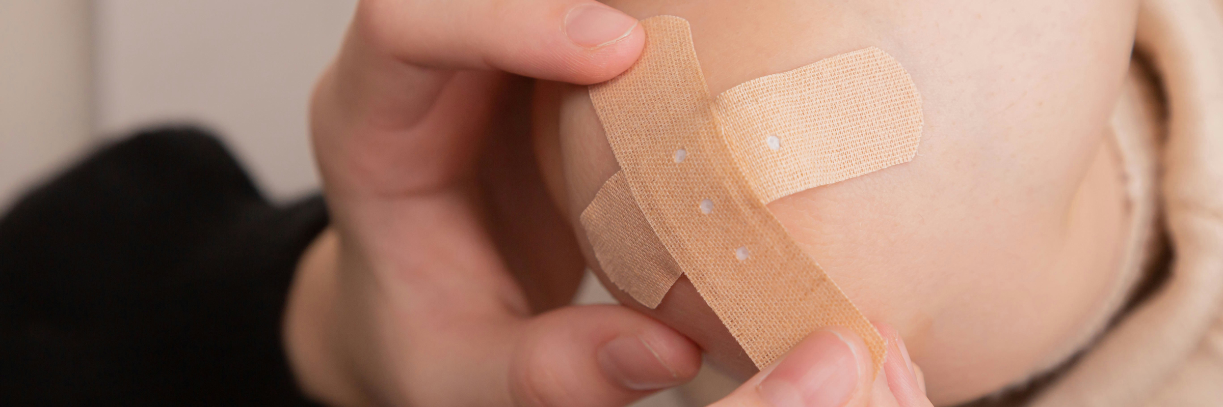 Zwei Wundpflaster werden kreuzförmig auf ein Knie geklebt.